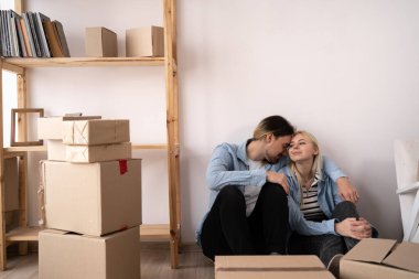 Yeni evlerinde karton kutuları olan mutlu genç bir çift, yorgun koca ve karısı yeni bir apartmanın zemininde oturuyor, taşınıyorlar ve ev satın alıyorlar.