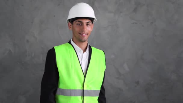 年轻的穆斯林建筑师戴着建筑商的安全帽 带着孤独的背景 高兴的面庞 交叉着双臂 看着相机 戴白色头盔的阿拉伯工程师积极的人 — 图库视频影像