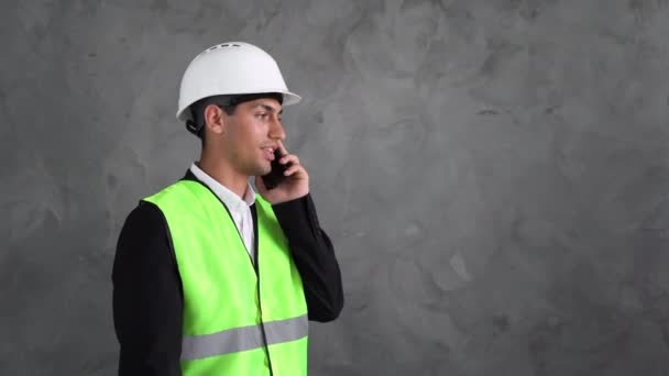 穆斯林工程师在智能手机上说话 拿着手机画画的男人建筑 工程戴着灰色背景的白色头盔的家伙 电话咨询客户 — 图库视频影像