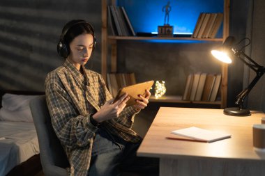 Asyalı kız öğrenci akşamları dijital tablet bilgisayar ve kulaklık kullanır, film izler ya da gece evde müzik dinler.