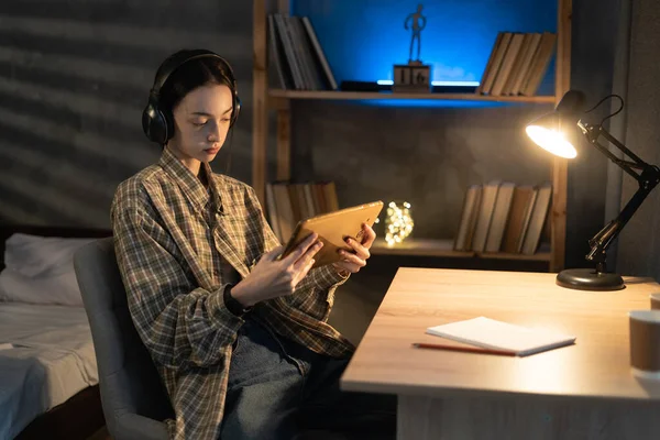 Asyalı kız öğrenci akşamları dijital tablet bilgisayar ve kulaklık kullanır, film izler ya da gece evde müzik dinler.