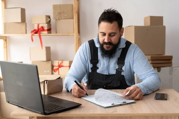 Indian bearded business men use laptop checking customer order online shipping boxes at home. Starting Small business entrepreneur SME freelance. Online business, work at home concept.
