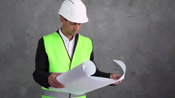 阿拉伯英俊的工程师或建筑师站在水泥墙的后面 手里拿着一张画着图画的单子 戴着白色硬礼帽的工人在做一个项目 — 图库视频影像