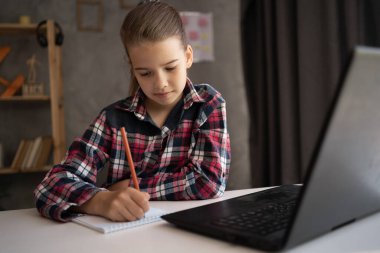 Gülümseyen küçük kız el yazısı çalışması, evde dizüstü bilgisayar kullanımı, küçük çocuk internet dersi veya bilgisayar dersi alıyor, evde eğitim kavramı