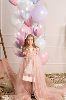 Şen şakrak giyinmiş, hava balonları taşıyan, bayramı ya da doğum gününü kutlayan, pembe stüdyo geçmişine karşı duran, neşeli bir kız. Çocuklar ve kutlama konsepti