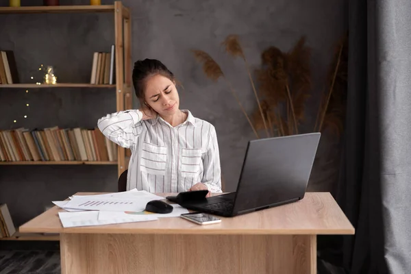 Business woman with neck ache, young woman suffering from neck pain in home office, massaging her neck while working