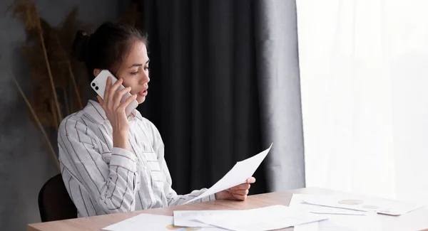 young woman with mobile phone and papers working at home office and calling on smartphone. remote job, technology and people concept, banner, place for text