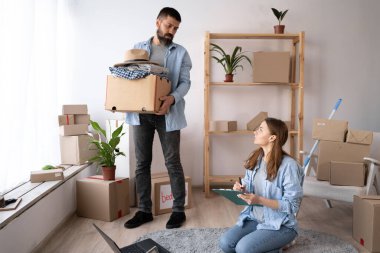 Genç çift yeni eve taşınmadan önce kontrol listesi kullanarak eşyaları paketliyor ve kontrol ediyor..