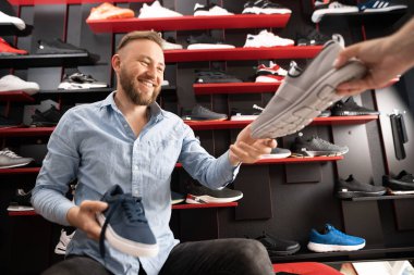 Yürüyüş için ayakkabı seçen adam modern spor mağazasının soyunma odasında oturuyor. Satıcı, alıcının spor ayakkabısı seçmesine yardım ediyor.