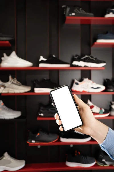 smartphone with sport shoes on shelves in sneakers shop modern sports store background. mobile phone with blank screen for your advertisment.