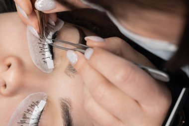 Güzellik salonunda cımbızla kirpik uzatma prosedürü uygulayan genç bir kadın.