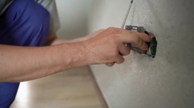 Elinde tornavida tutan elektrikçi adamın elleri konut elektrik sisteminde fiş üzerinde çalışıyor. Ev onarımında beyaz havalandırma prizi takıyor. Kapatın.