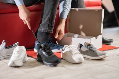 Spor ayakkabılarını deneyen genç bir adam, modern spor malzemeleri mağazasının soyunma odasında oturuyor.