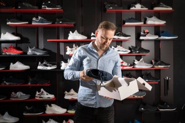 Spor mağazasında spor ayakkabısı seçen genç bir adam, butikte ayakkabı alışverişi yapan biri.