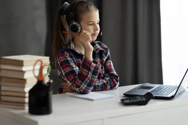 Portrait of student learning online with headphones and laptop taking notes while sitting at her desk at home. study remote use laptop online teacher communication chatting. Home schooling concept.