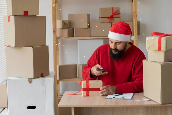 Indian man entrepreneur small business owner is packing gifts box at home in a small office. Santa prepares boxes for shipment. Big sale for Christmas. home office is the seller of online store. start-up