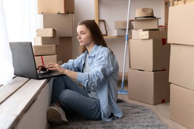 Young girl sitting on the floor using laptop computer wireless internet, moving to a new house, moving day concept
