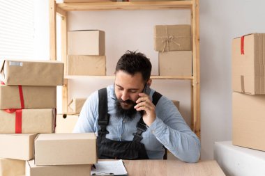 İnternetteki sakallı adam müşterinin siparişlerini onaylıyor. E-ticaret erkek işyeri sahibi, depo deposunda kutu kargo için telefon kullanıyor. KME kavramı