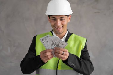 Güvenlik kaskı takan genç bir Arap mühendis. Arka planda dolarlar var. Yükseltilmiş elle ödeme, inşaat konsepti.