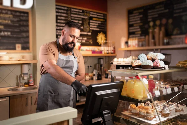 Male Indian barista or owner at counter using cashbox computer in cafe store checking client\'s order. Waiter in apron working in coffee shop. small business, people and service concept