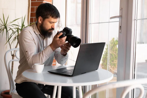 Kafede dizüstü bilgisayar ve dijital kamerayla çalışan yaratıcı fotoğrafçı. Profesyonel gazeteci ya da serbest çalışan DSLR kamerasıyla fotoğraflara bakıyor.