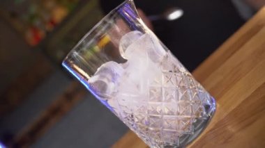 Barmen kokteyl bardağında yüzsüz bir kaşıkla buz karıştırır..