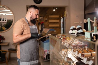 Modern kafe içinin barında dijital tabletle çalışan önlüklü yakışıklı kafe sahibi veya garson.