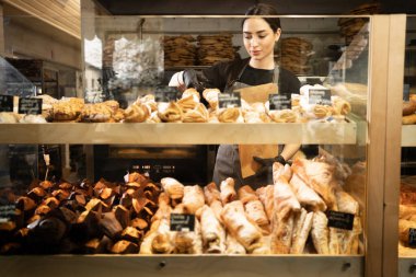 Young woman preparing pastry for sale in supermarket bakery department. Bakery female seller.
