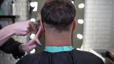 Machine haircut for handsome bearded man in barbershop.Confident guy sitting at beauty salon.