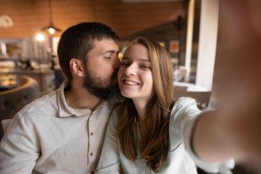 Smiling beautiful woman and her handsome boyfriend. Couple at their date in restaurant. Happy cheerful family. They taking Pov selfie at cafe and kissing