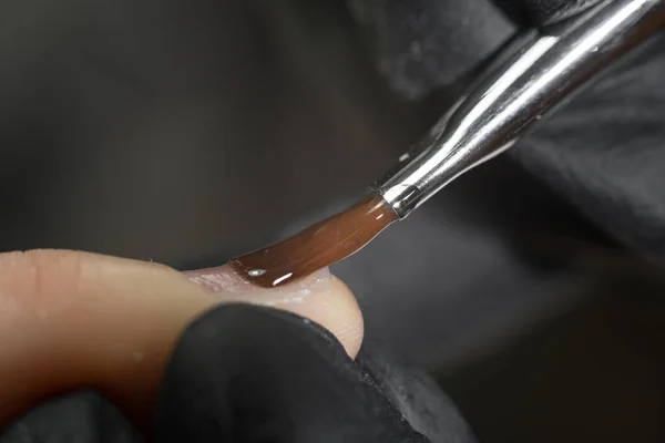 在黑色背景上用薄刷子修剪指甲的特写油漆 美容师在美甲沙龙里涂指甲油 有选择的重点 指甲油 造型凝胶 — 图库照片