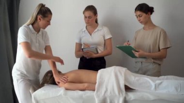 Sağlık masajı eğitimi konsepti. Bir kadın öğretmen el hareketlerini nasıl düzgün bir şekilde yapacağını öğretir, öğrenciler izler ve yazar. Boşluğu kopyala.