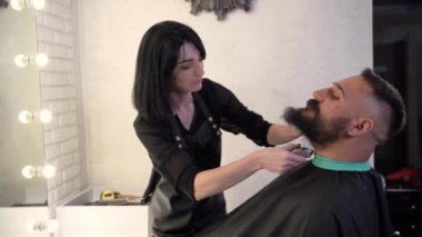 Sakallı ve bıyıklı yakışıklı hippi sakallı adam saç tıraşı olur ya da kuaförde kırpılır. Berber kadın berber dükkanında çalışıyor.