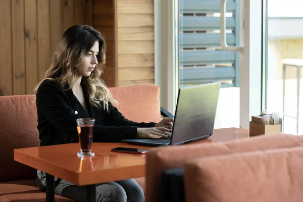 Serious young woman sitting in cafe working on laptop, charming freelancer girl thinking about new ideas while working with pc, technology or startup business concept