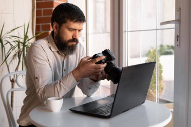 Kafede dizüstü bilgisayar ve dijital kamerayla çalışan yaratıcı fotoğrafçı. Profesyonel gazeteci ya da serbest çalışan DSLR kamerasıyla fotoğraflara bakıyor.