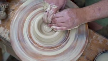 Dönen çömlekçi çarkı ve çanak çömlek, yukarıdan çekilmiş. Adamın biri çömlekçi çarkına kil kase yontuyor. Çamur eller. Çömlek ustası seramikçi el yapımı bir kil ürün üretiyor. İşlem