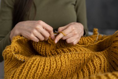 Close-up of female hands knitting wool sweater. Woman knits from thick yarn. Handmade clothes. The girl goes in for her hobbies. Knitting concept