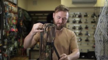Caucasian bearded man in a fishing tackle shop getting ready for a fishing trip. Bought a lot of gear. The concept for fishing is completely ready