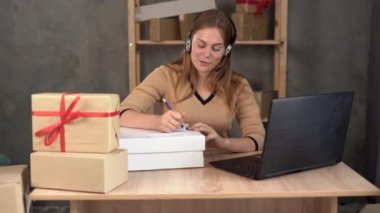 small business startup, small and medium business freelancer working with box, young smiling female call center operator with wireless headset headphones and microphone taking order online.