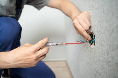 Elektrikçi, tornavida kullanarak duvardaki elektrik kablolarına bağlanıyor.