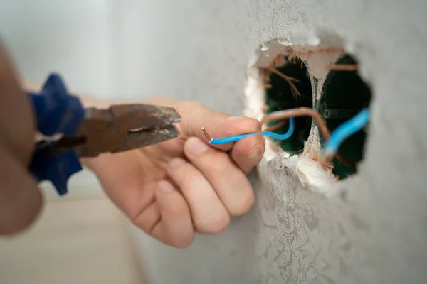 man works with electrical wires using tools, fixing socket at home, male household work with electricity, pliers and wire cutters in man's hands, electrician working with wire