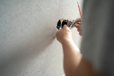 Close-up of electrician hands with screwdriver installing wall socket. Electrician wiring a new build.