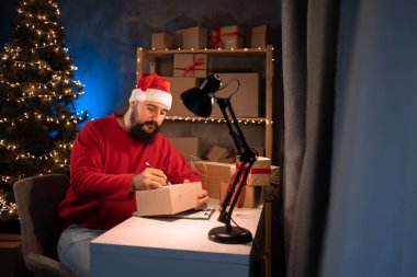Small and medium business startup concept bearded male Hindu entrepreneur, small business owner, packing goods, preparing for shipping. good earnings during the christmas sale. santa claus costume