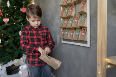 Duvarda asılı duran takvim. Çocuk hediyeyi açar. Noel çocukları eğleniyor. Şekerli el çantaları. El yapımı kış sürprizi