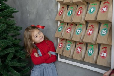 Duvarda asılı duran el yapımı takvim, şekerli el işi çantaların yanında duran kız, çocuklar için bayram eğlencesi, kış gelenekleri konsepti