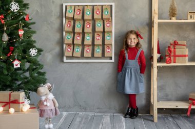 Noel gelenekleri konsepti, takvimi olan bir çocuk, duvarda şekerlerin asılı olduğu el işi paketler, çocukların Noel neşesi.