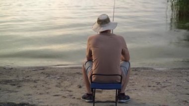 the view from the back is a man fisherman at dawn on the lake catching fish with a bait. sits on a chair and waits for a bite. Fishing holiday concept. copy space