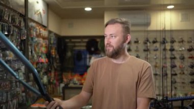 young bearded caucasian male fisherman in a fish tackle shop chooses a landing net for fishing, compares two options and buys the best one. close-up