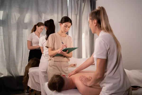 Teacher helping student training to become masseuse, women doing back massage to patient, wellness massage training concept