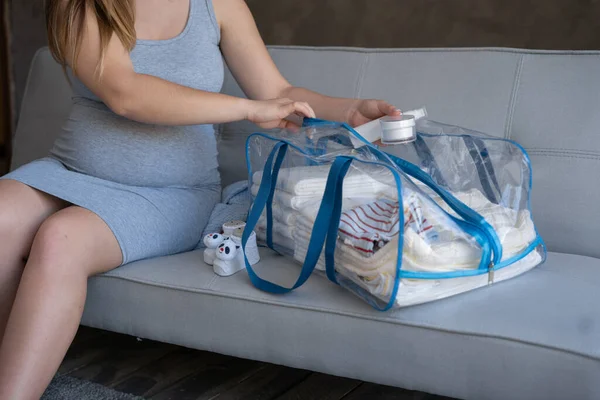Pregnant woman packing bag for maternity hospital at home. pregnancy, childbirth and people concept
